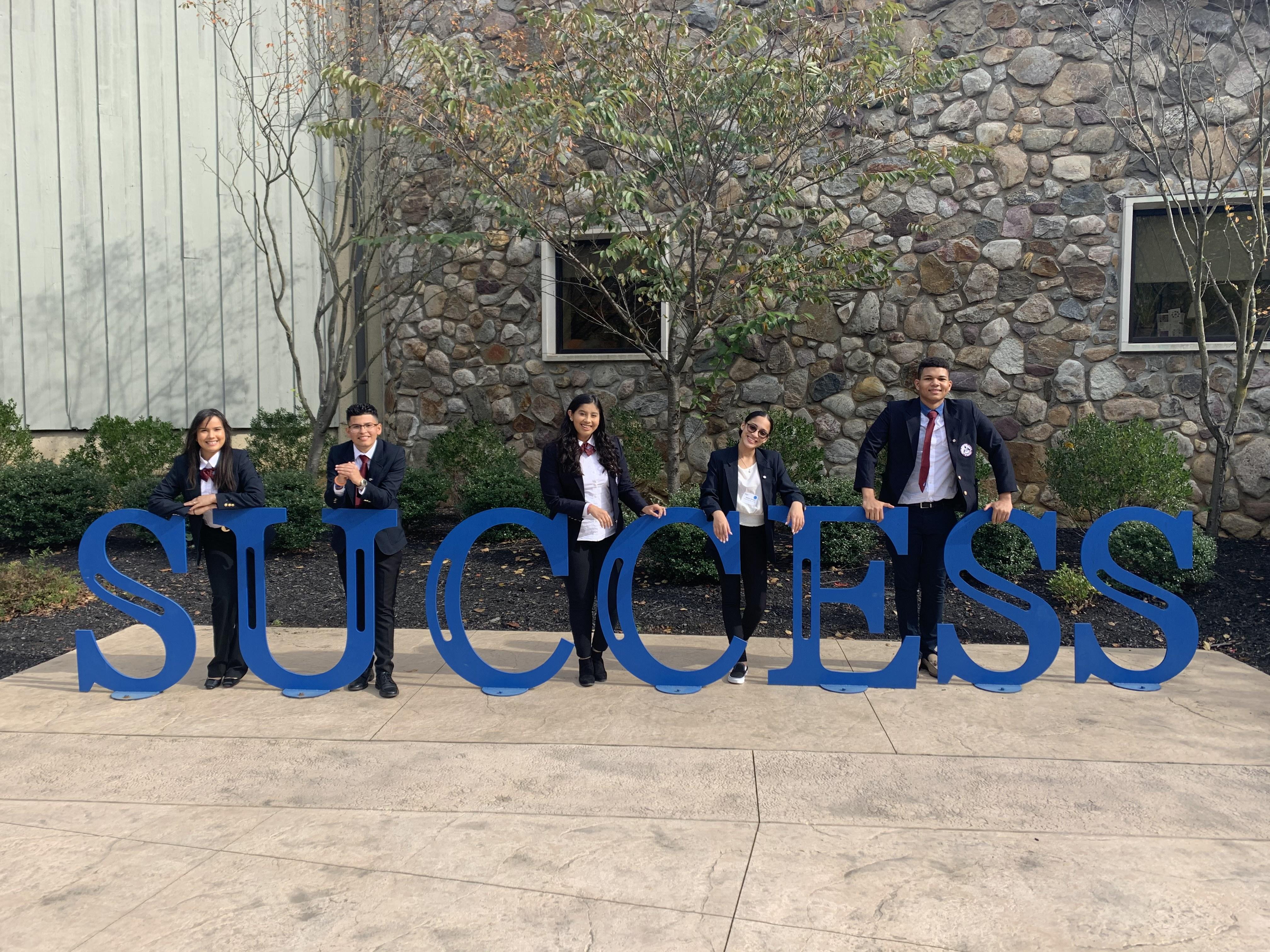 students standing by large blue letters that spell sucess